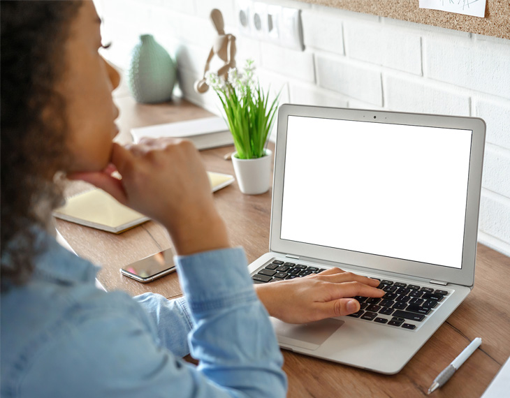 Individual with curly hair sitting at a desk, using a laptop with a blank screen. - International Hotel School