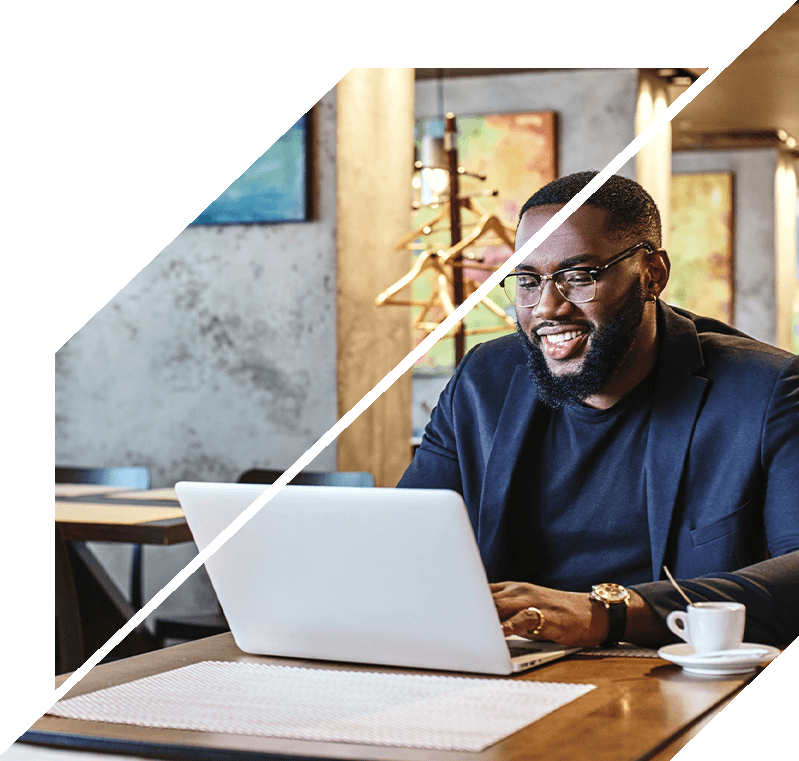 Man with glasses working on a laptop at a table in a modern indoor setting.