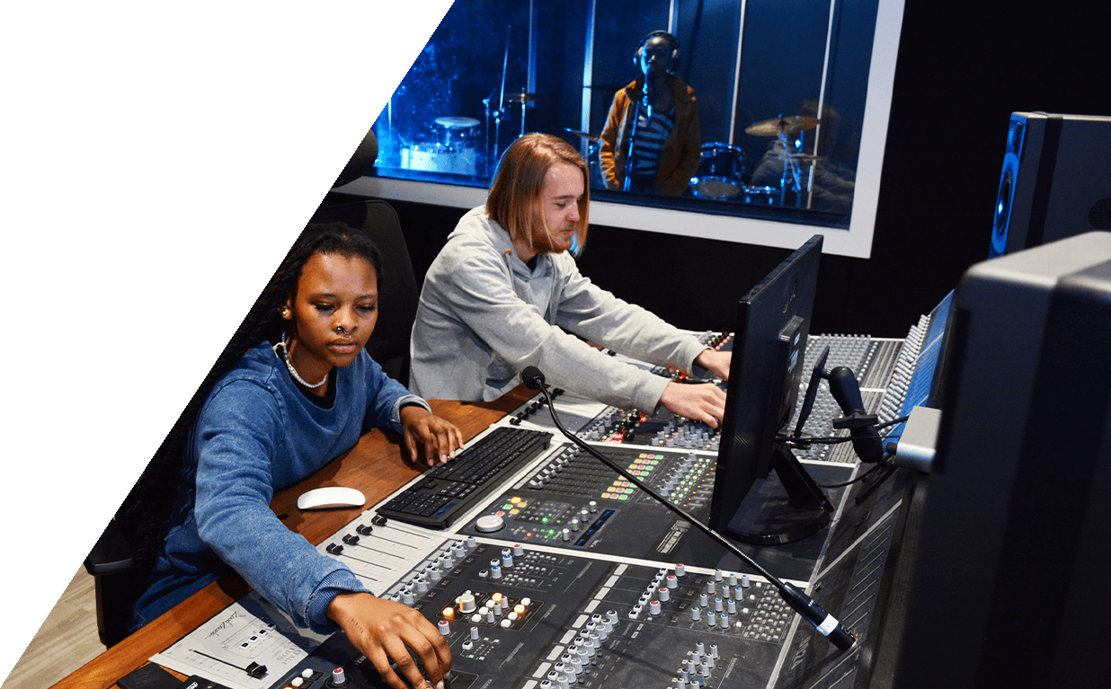 Two individuals working at a music production studio with mixing equipment and a visible recording area.