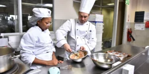 Chef instructing a student in a professional kitchen during a cooking class. - International Hotel School
